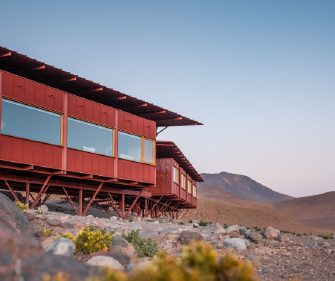 A modern lodge set in a dry, rocky landscape at dusk.
