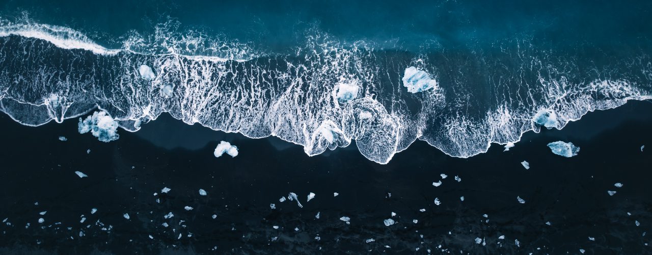 http://An%20aerial%20view%20of%20dark%20ocean%20water%20where%20waves%20crash%20against%20ice%20fragments%20scattered%20along%20the%20shoreline,%20creating%20a%20striking%20contrast%20of%20white%20and%20deep%20blue.