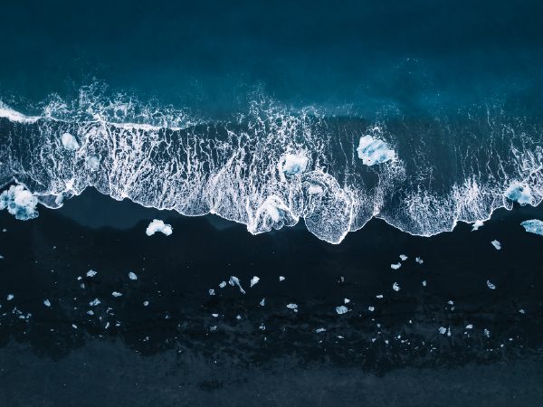 http://An%20aerial%20view%20of%20dark%20ocean%20water%20where%20waves%20crash%20against%20ice%20fragments%20scattered%20along%20the%20shoreline,%20creating%20a%20striking%20contrast%20of%20white%20and%20deep%20blue.
