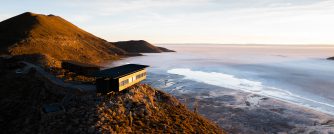 A modern lodge clings to a hillside overlooking vast salt flats in golden sunset light.