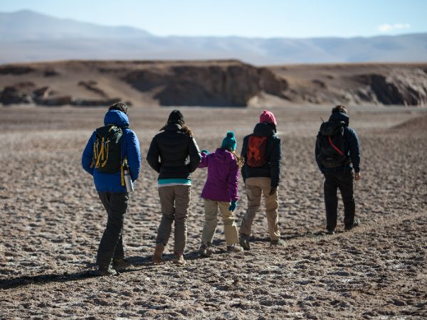 Adults and children walk together across a vast desert plain with hills in the distance in Atacama