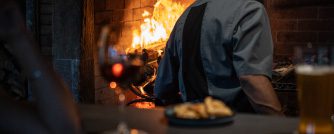 Chef cooking over an open fire in a Patagonian restaurant with local food and craft beer in the foreground