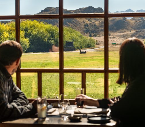 Guests dining at a Patagonia lodge restaurant while looking out over grasslands and mountains through large windows