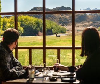 Guests dining at a Patagonia lodge restaurant while looking out over grasslands and mountains through large windows