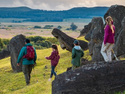 A group with children walks among large rock formations in an open, green landscape in Rapa Nui