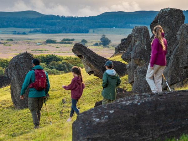A group with children walks among large rock formations in an open, green landscape in Rapa Nui