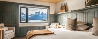 Cozy hotel bedroom with large window framing panoramic views of Torres del Paine mountains