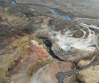 Aerial view of an active geothermal hot spring venting steam across Iceland's volcanic Highland landscape