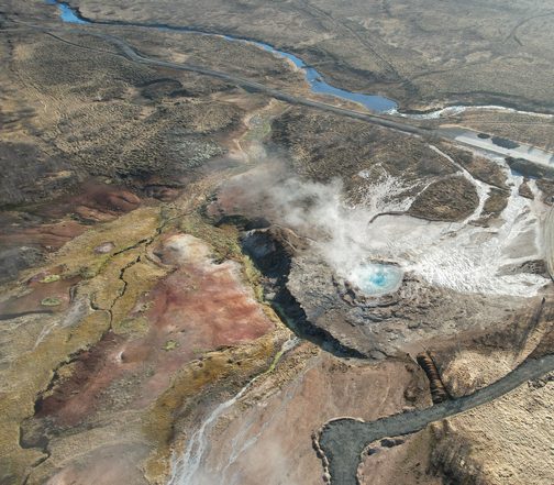 Aerial view of an active geothermal hot spring venting steam across Iceland's volcanic Highland landscape