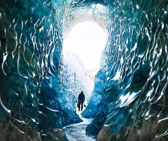 Explorer inside a blue ice cave in Vatnajökull glacier, Iceland — turquoise glacial walls and natural ice tunnel