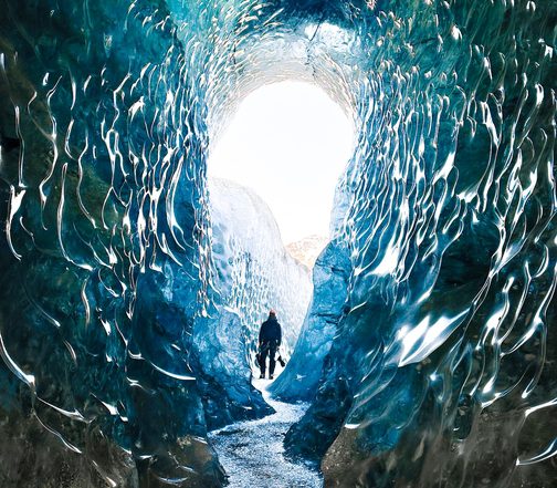 Explorer inside a blue ice cave in Vatnajökull glacier, Iceland — turquoise glacial walls and natural ice tunnel